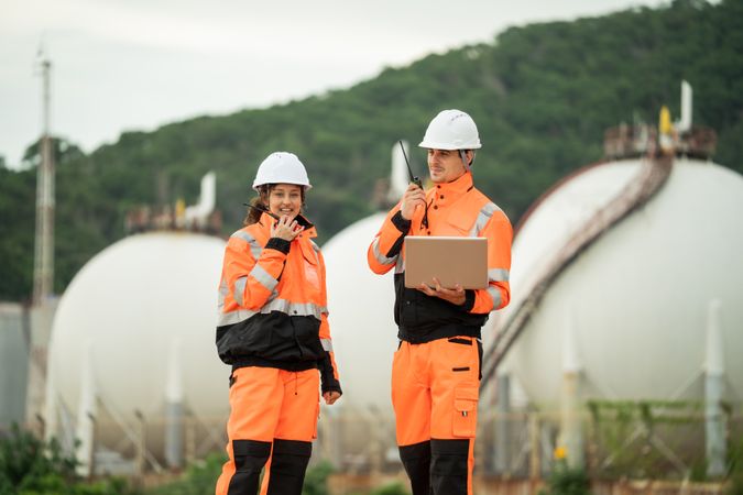 Two engineers are working at an industrial site near spherical gas storage tanks.