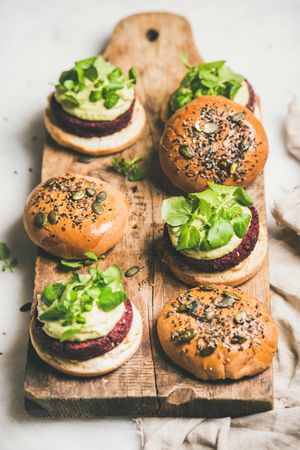 Fresh vegan burgers on seeded buns arranged on wooden bread board