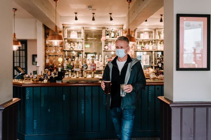 Man in facemask collecting pints of beer from pub