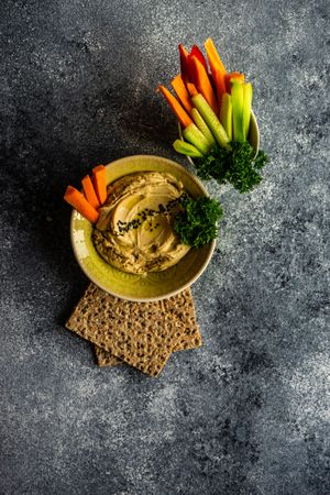 Top view of creamy hummus and chopped vegetables on grey kitchen counter with copy space