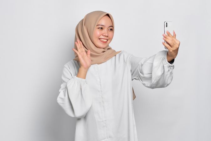 Asian Muslim woman waving at phone during video call