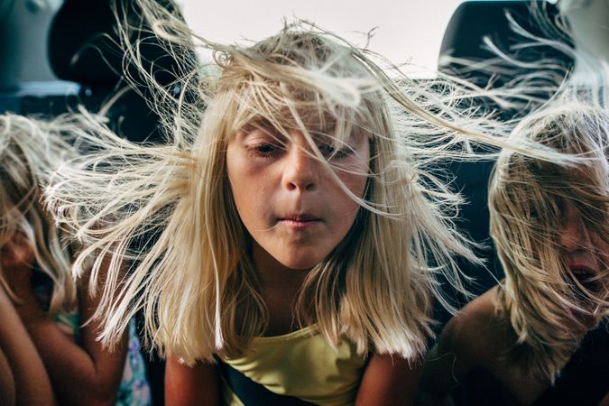 Three blond siblings sitting in vehicle with wind in their hair