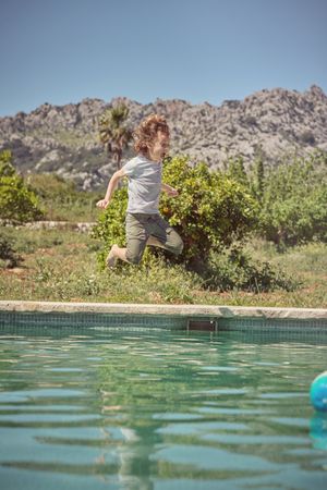 Cheerful boy jumping in swimming pool during summer vacation