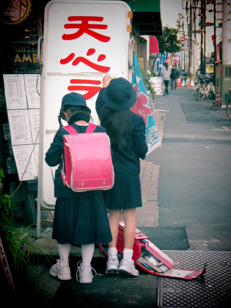 Back view of two girls in school uniform standing on sidewalk