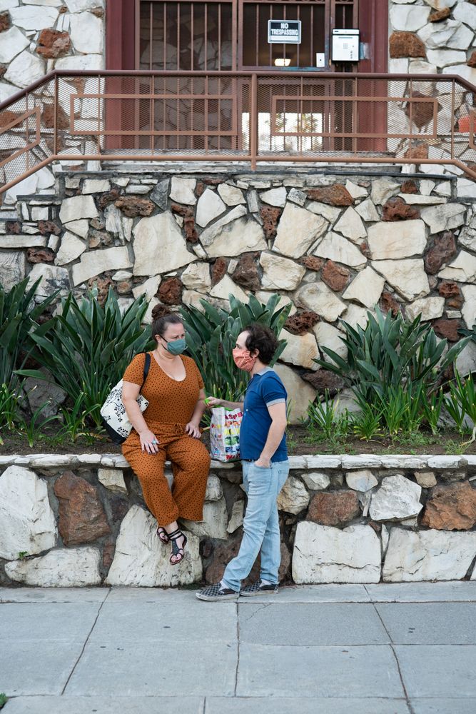 Man and woman sitting on stone wall with groceries and talking