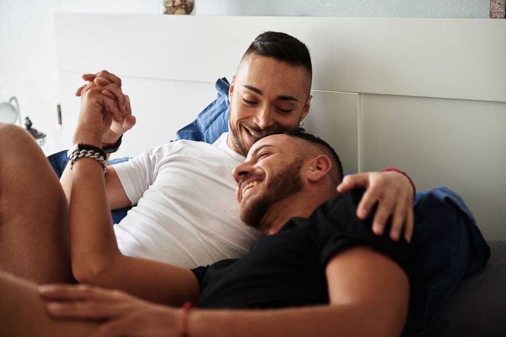 Smiling gay couple hugging on bed