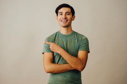 Happy Hispanic male pointing left in neutral room, copy space