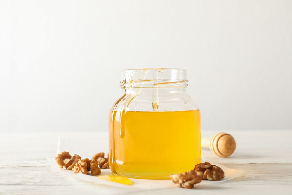 Walnuts, dipper, parchment and glass jar with honey on neutral background, copy space