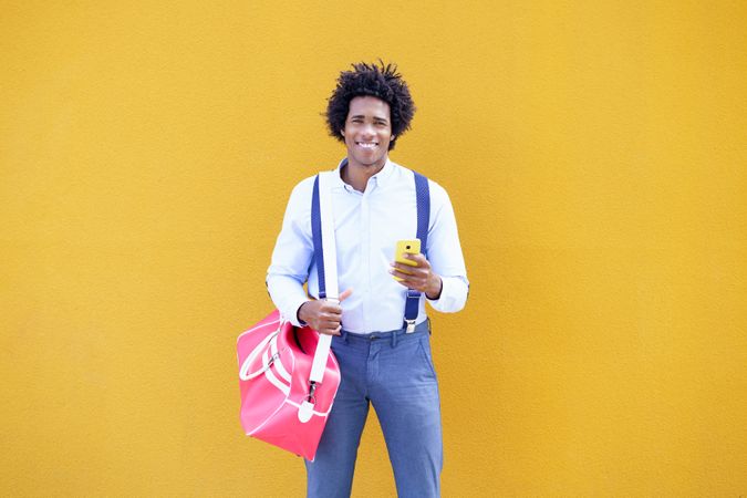 Guy with curly hair wearing shirt and suspenders in front of yellow wall