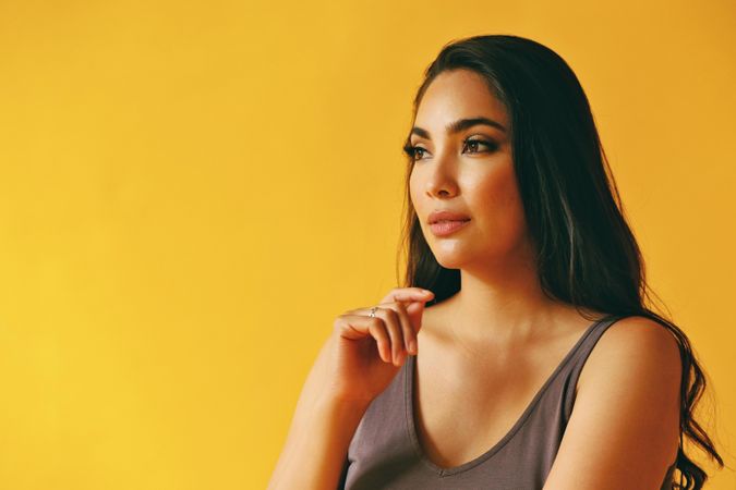 Thoughtful Hispanic woman looking away from camera in yellow room, copy space