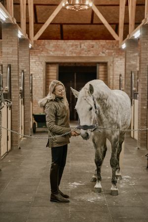 Woman hugging horse with long mane in face in stable
