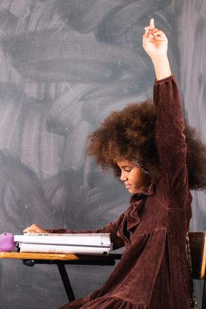 Black girl with raised hand in classroom during lesson
