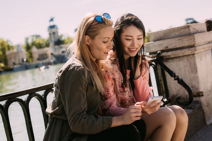 Multiethnic friends using smartphone on embankment