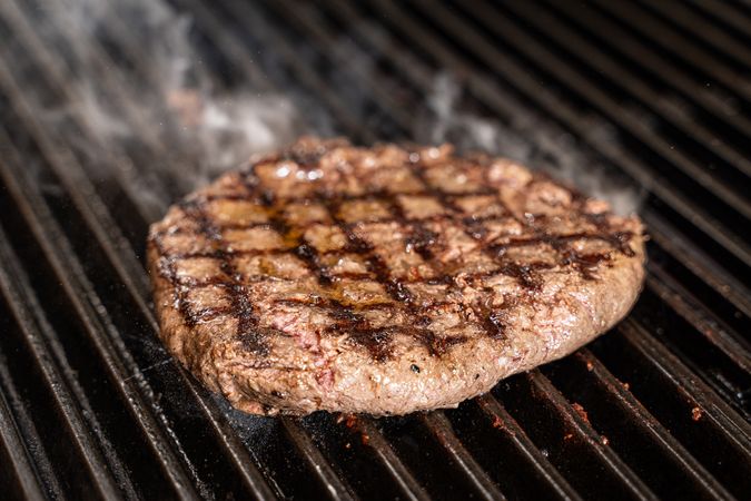 Juicy grilled beef patty with smoke rising on barbecue grill
