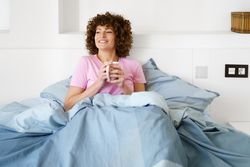 Happy woman lounging in blue bed with cup of coffee