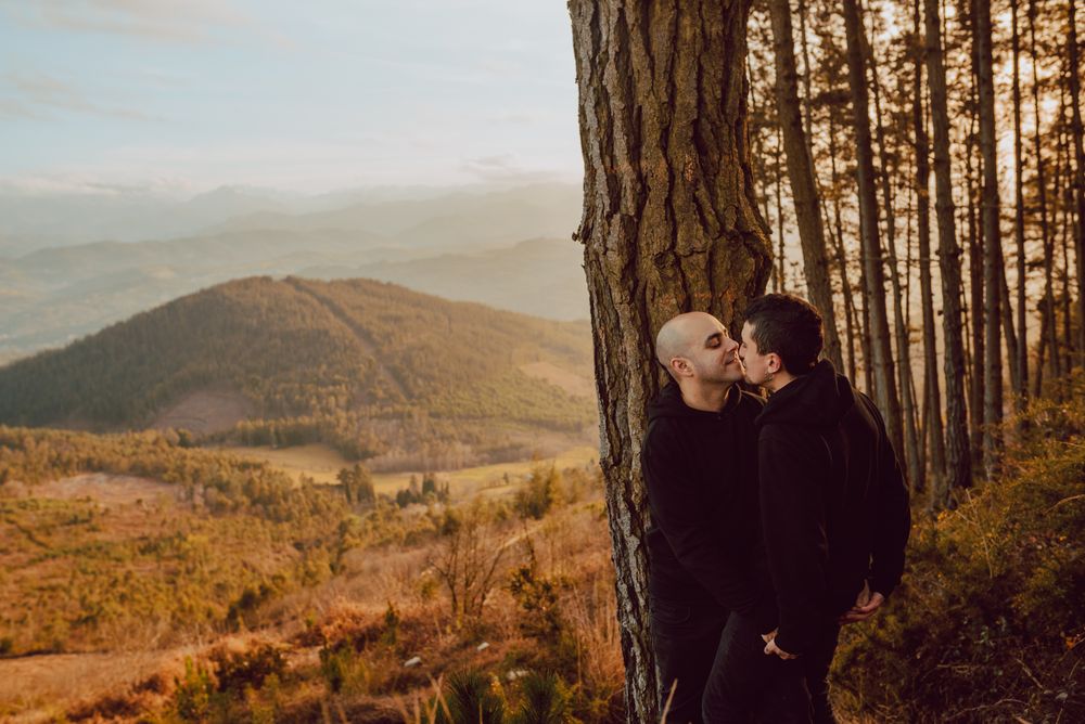 Smiling men hugging near tree in forest on hill