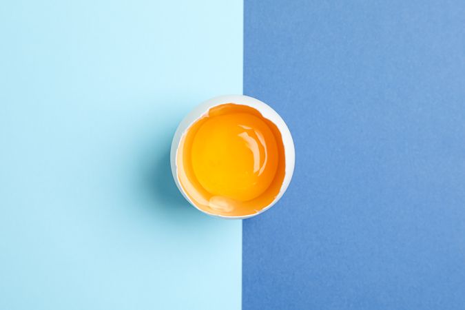 Half broken egg with yolk on to color background, space for text and top view