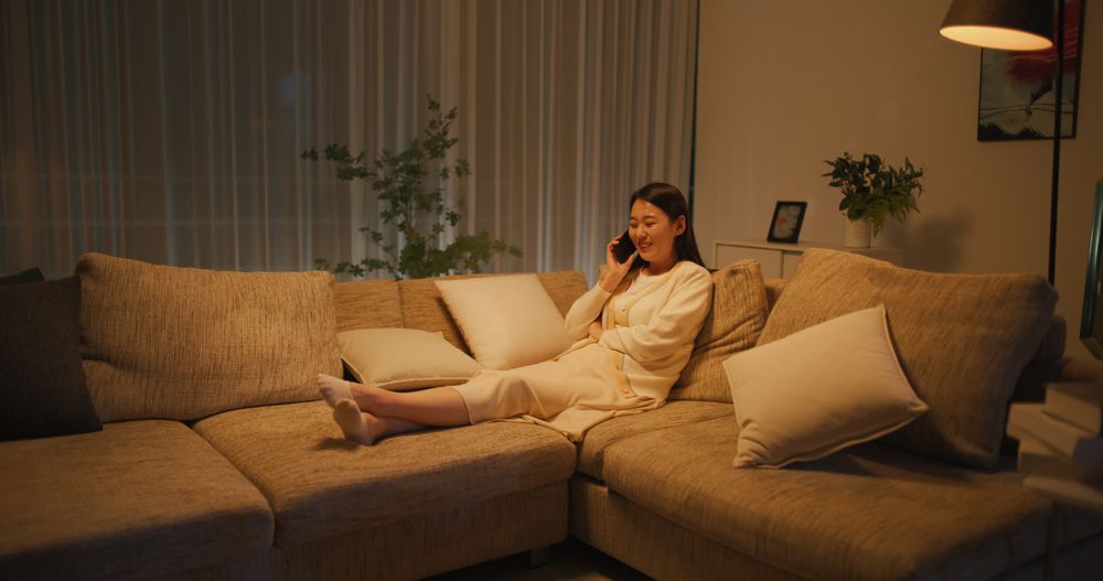 Relaxing on a Couch in the Evening in a Cozy Apartment, Smiling South Korean Woman is Having a Phone Conversation