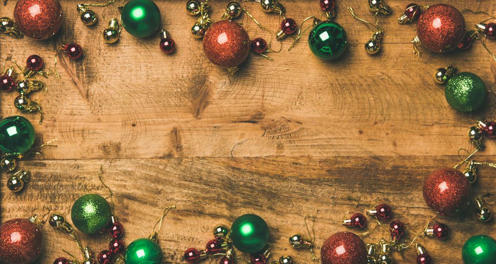 Green, red, and gold tree ornaments arranged on wooden board with copy space in center
