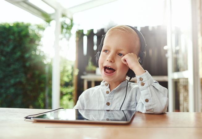 Happy blond boy using headphones listening to something on digital tablet