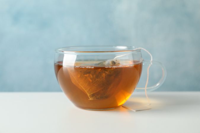 Cup of tea with tea bag on plain background, space for text