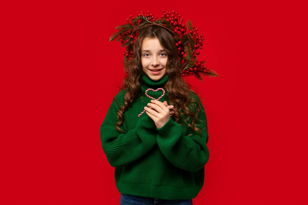 Girl in green sweater holding two candy canes shaped heart