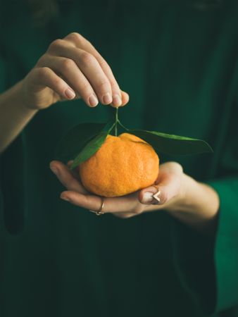 Woman in green holding tangerine, copy space