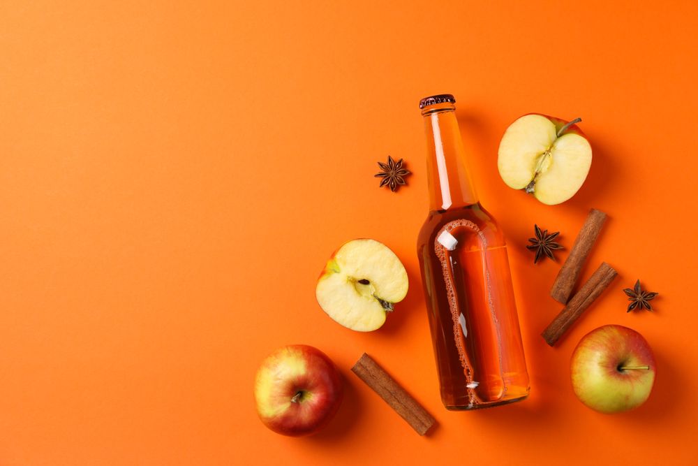 Composition with cider, apples and cinnamon on orange background
