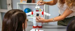 Teacher in a robotics class explaining how connect solar panel on recycled toy robot