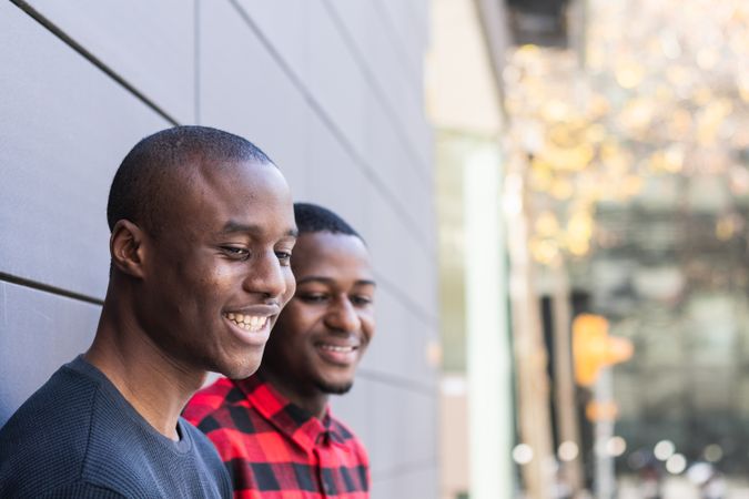 Side view of happy Black male friends against gray wall