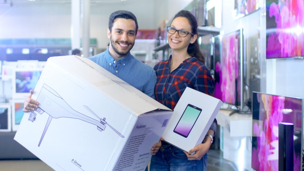 In the Electronics Store Happy Young Couple Poses with Newly Purchased Drone and Tablet Computer.