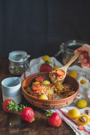 Person holding wood spoon with granola and strawberry from bowl