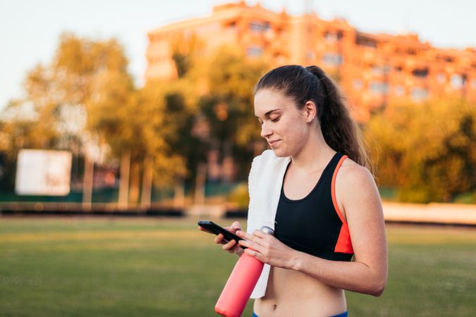 An athletic woman resting with her smartphone after running.