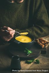 Man with stubble eating warm yellow soup from dark bowl with toast 5akqGb