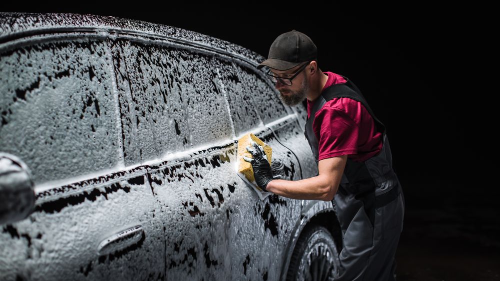 Portrait of an Adult Man Working in a Detailing Studio, Prepping a Factory Fresh Electric SUV for Maintenance Work and Car Care Treatment.