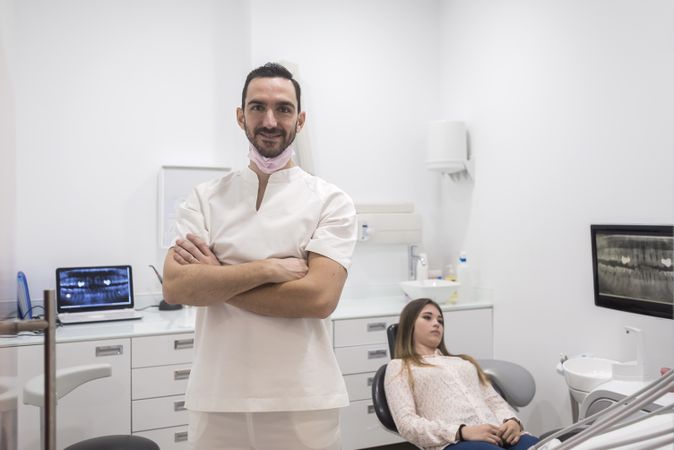 Smiling male dentist pictured in his office with patient in background