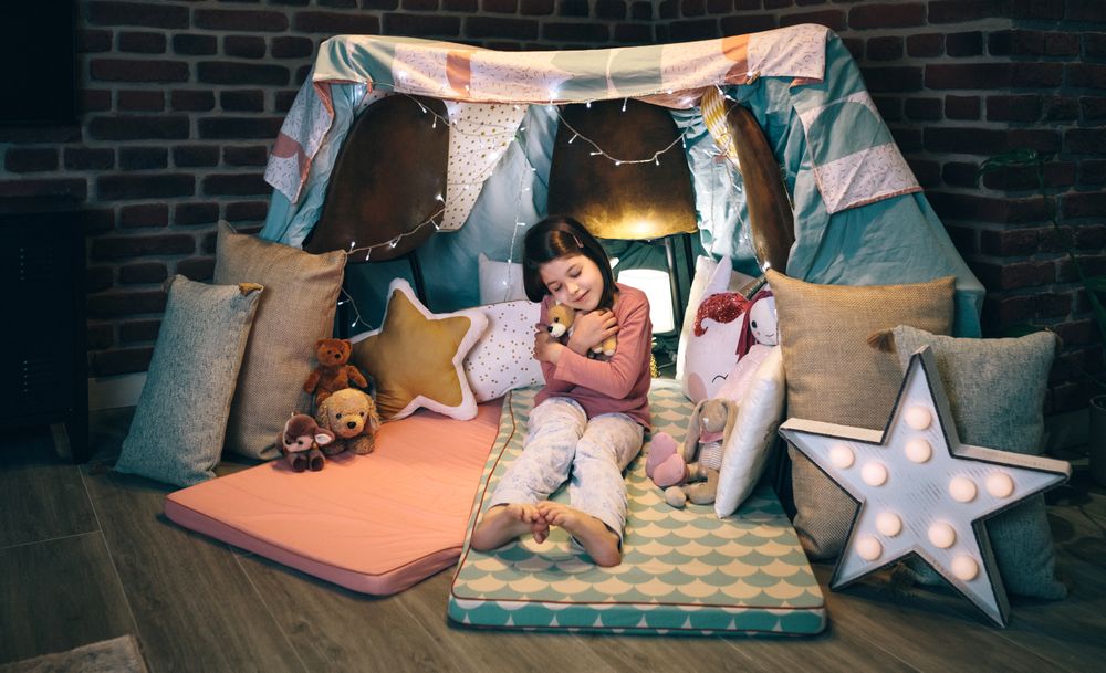 Girl hugging stuffed doll playing in a diy tent at home