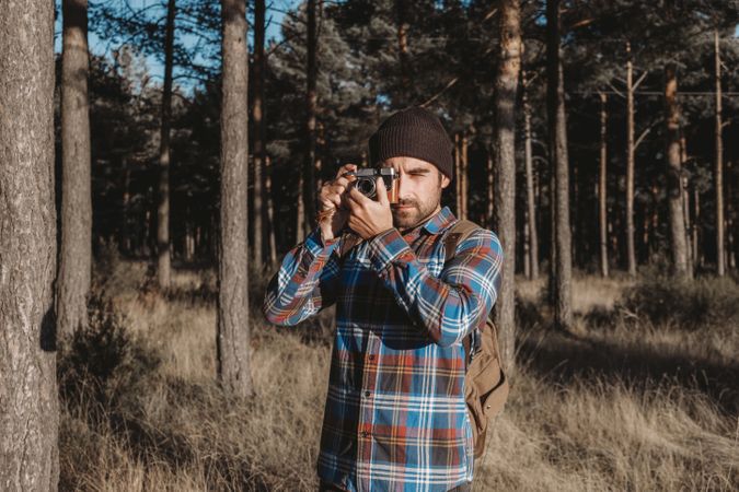 Confident photographer taking picture with camera in sunny forest