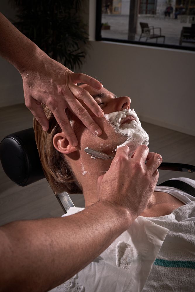 Unrecognizable barber shaving beard of man
