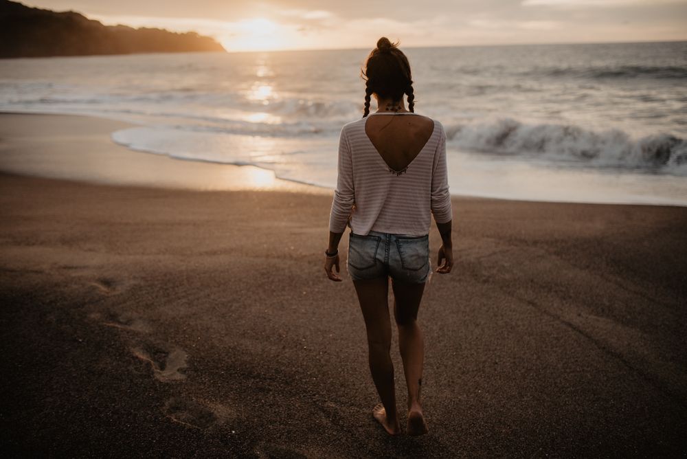 Anonymous female walking towards waving sea on sunset