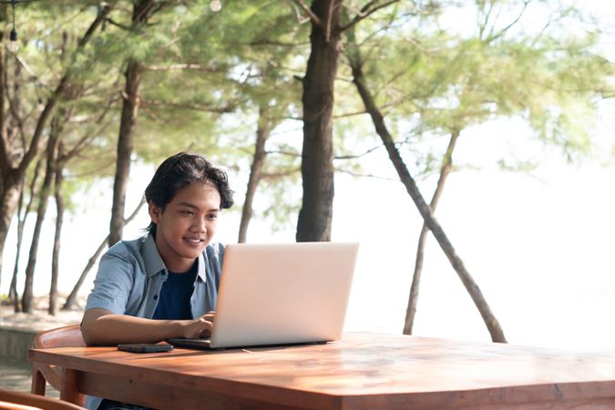 Happy Asian Young businessman work at outdoor with laptop. Concept of remote and freelance work. Young successful man wearing casual blue cloth.