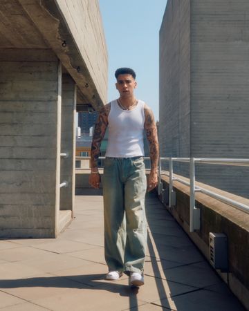 Front of man in vest and jeans walking among concrete structures