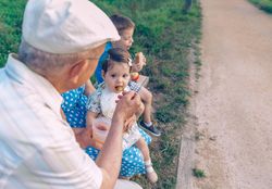 Back of older man feeding baby girl sitting in a bench