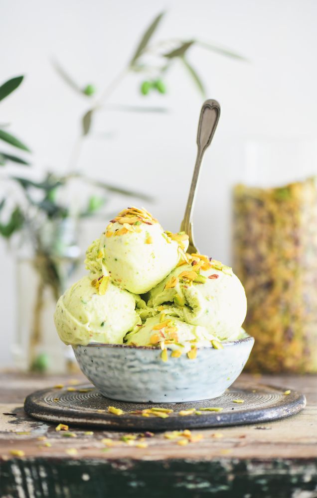 Bowl of melting pistachio ice cream with spoon, and light background with leaves and glass jar