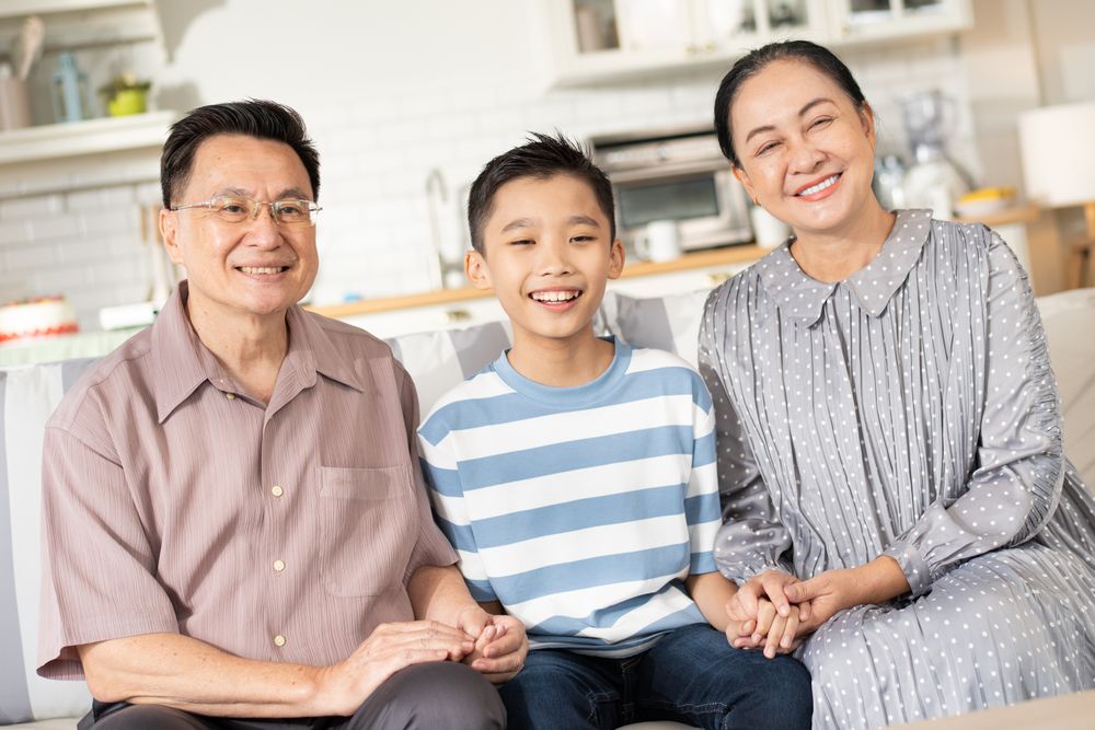 Happy Asian grandson and grandparents relax sitting on couch in the living room