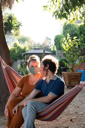 Woman smiling at man while sitting together in hammock in garden