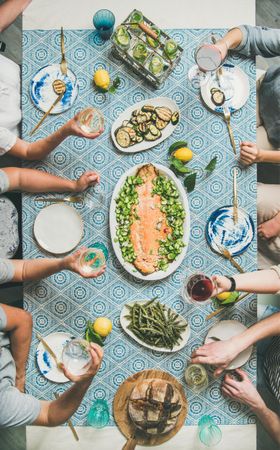 Group of people at blue patterned table with fish, and vegetable side dishes, vertical composition