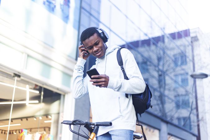 Young Black man standing in the street with bike and checking his phone