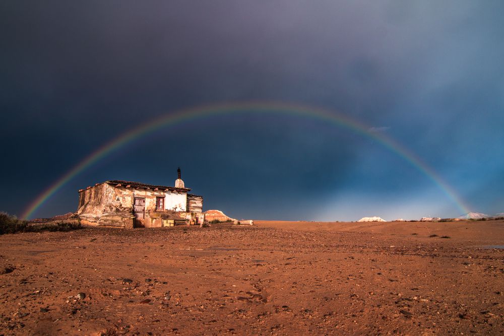 Lonely house in desert and rainbow in sky