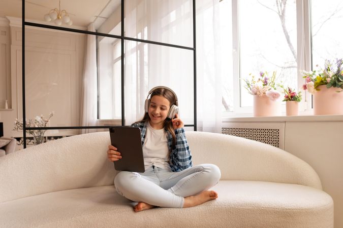 Teen girl enjoying tablet and headphones comfortably at home.